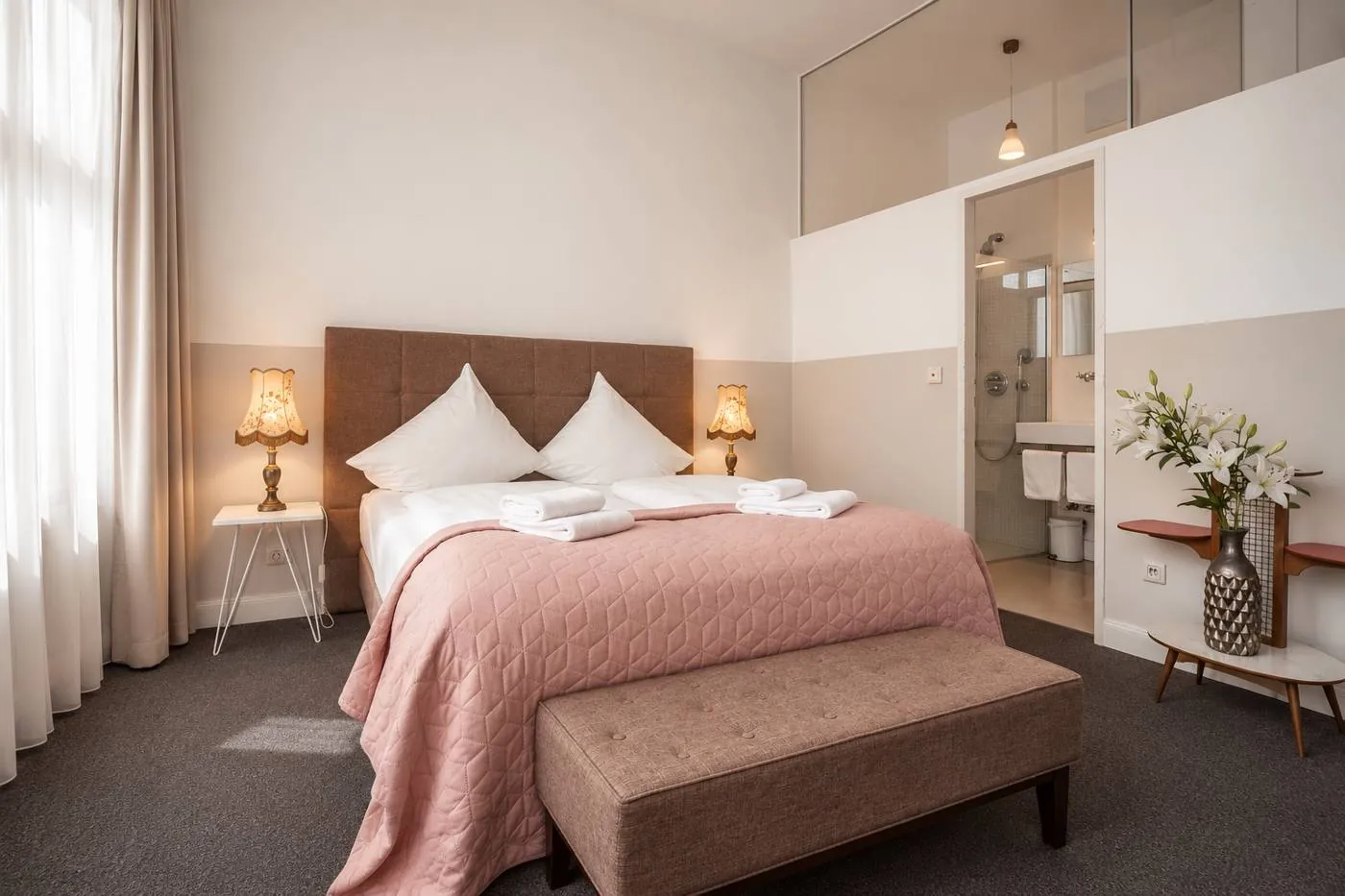 Deluxe Zimmer mit Bett, Nachttischlampen und Blick ins Bad