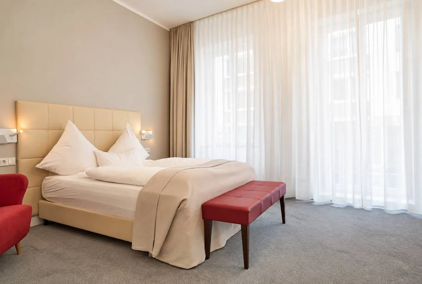 Zimmer mit Doppelbett, roter Polsterbank und bodentiefen Fenstern